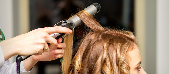 发型师在美容院为长棕色头发的年轻女子做卷发卷发和卷心铁客户造型女性女孩造型师理发师卷发器发型设计服务沙龙图片