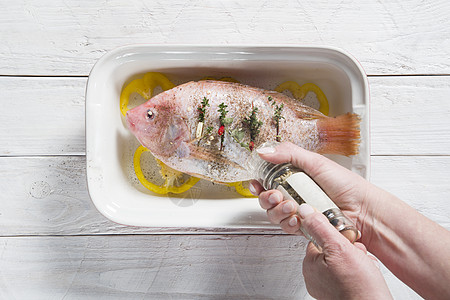粉红罗非鱼和蔬菜在烤盘中 手对鱼的香料图片