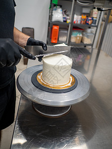 厨师蛋糕 用奶油淇淋和烟雾及用具来润滑一个霜冻的蛋糕制作者黄油水分手工旋转装潢奶油工作美食家刮刀图片