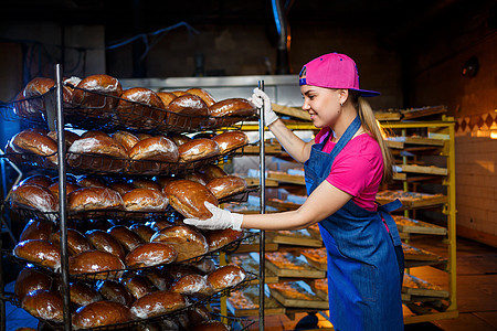 专业面包师  一位身穿牛仔裤围裙的年轻漂亮女性在面包店或面包店的背景下拿着新鲜面包 烘焙食品 面包生产食物包子零售女孩孩子咖啡店图片