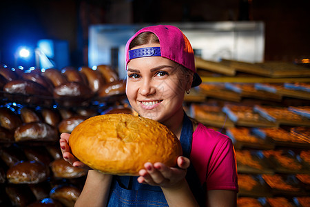 一个面包师女孩的画像 她手里拿着面包 放在面包店货架的背景上 贝克的手拿着面包 面包的工业生产女孩厨房工作男人女性烤箱情感面包师图片