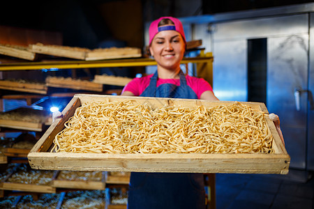 这个女孩从事意大利面条的生产 做面条 面食厂 意大利面的阶段生产 生面条 拿着一盒意大利面的工人工作木板同事面粉电脑职业微笑女性图片