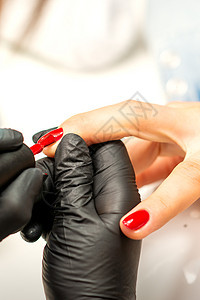 在美容院的一只雌性指甲上涂着红色清漆 穿着橡皮黑手套的美甲师傅贴近了她的身影身体美甲师女士优雅皮肤工具抛光服务成人工作图片