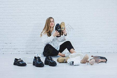 身着白色衬衫和黑色裤子的时髦服装 微笑着的快乐美丽的年轻女人坐在鞋子中间的地板上 为自己选择一双新鞋短剑时尚衣柜房间女孩女性店铺图片