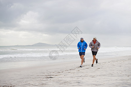 和朋友在沙滩上晨跑 两个男人在一个阴天的早晨一起沿着海滩慢跑的全长镜头图片