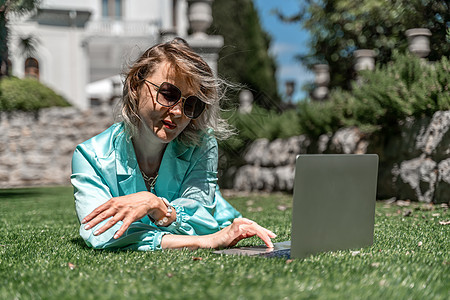 一位美丽的年轻女子 金发卷发戴眼镜 穿着蓝裙子 在大自然的草地上坐着 用笔记本电脑女孩地面手机技术稻草旅游房子学生金发女郎沙发图片