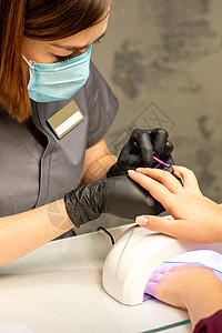 专业美甲 一位美甲师正在一家美容院用紫色指甲油为客户的女性指甲上色 特写 美容行业概念刷子抛光橡皮沙龙治疗凝胶紫外线女孩工作手指背景图片