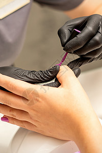 专业美甲 一位美甲师正在一家美容院用紫色指甲油为客户的女性指甲上色 特写 美容行业概念化妆品奢华治疗女士美容师沙龙刷子温泉手指搪图片