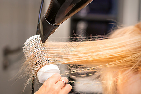 在理发厅用黑色洗发机和白圆刷子 擦干金发直发 特写吹风机烘干机女性享受烘干理发师美容师梳子染色发型图片