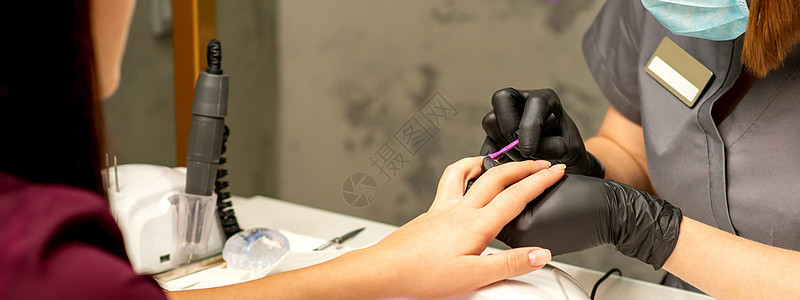 专业美甲 一位美甲师正在一家美容院用紫色指甲油为客户的女性指甲上色 特写 美容行业概念全景搪瓷美容师横幅刷子成人抛光艺术工具凝胶图片