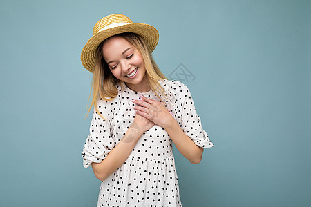 身着散装服 墨镜和草帽的年轻美丽可爱快乐金发女郎照片 在蓝色背景上与复制空间隔绝 
