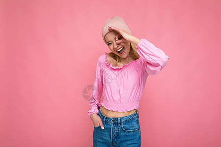 照片中 美丽快乐 风趣幽默的年轻金发女性被隔离在粉红色背景墙上 戴着时髦的粉红色帽子和粉红色衬衫 看着相机 摆出 ok 手势图片