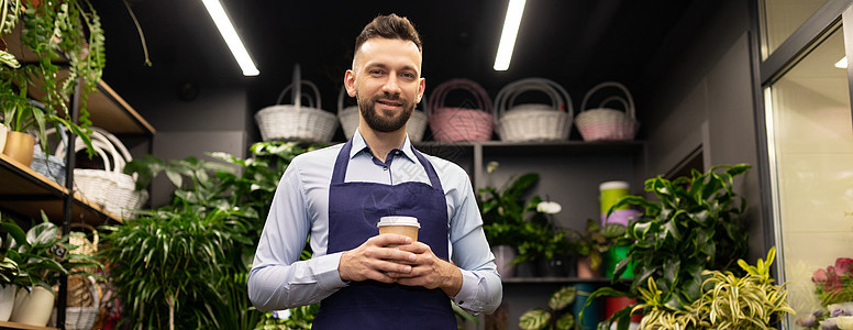 一位手里拿着一杯咖啡的成功男花商站在花店里 面带微笑地看着镜头图片