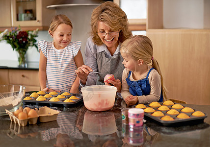 教她的孙子宝贵的厨房技能 两个小女孩在祖母的帮助下在家里烤纸杯蛋糕图片