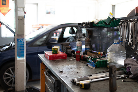 一张金属桌的照片 上面有用于工作和修理汽车的工作工具 背景是服务站一辆蓝色客车正在用敞篷修理车库车轮兜帽机器轮子引擎盖轮胎车辆乘图片