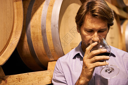 一个英俊的成熟男子 站在酒窖里 喝着一杯红葡萄酒图片