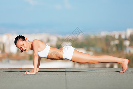 穿着运动服在屋顶做俯卧撑的年轻女性的肖像 - 她是个有魅力的年轻女子图片