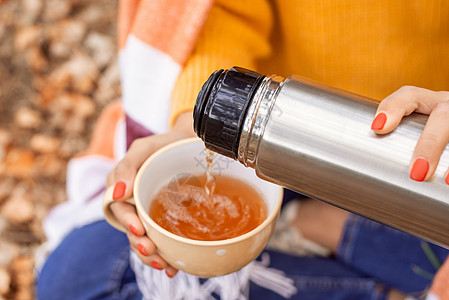 坐在户外的人和从温热中倒茶水到白色杯子的人图片