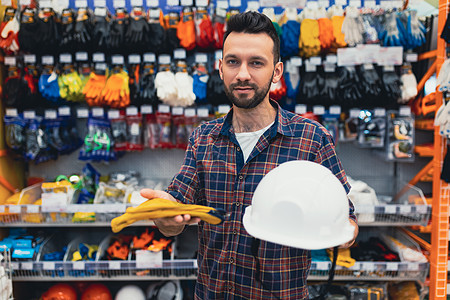 一家五金商店的男性建筑商选择硬帽和防护手套图片