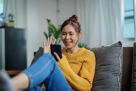 一位坐在沙发上手持智能手机的年轻亚洲妇女肖像家庭生活音乐摄影衬衫技术女性会议全景情感客厅图片