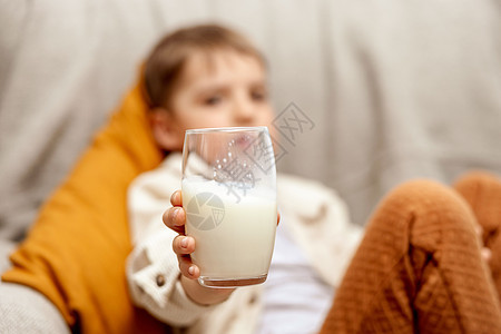 可爱的小男孩坐在家里的沙发上喝牛奶 玻璃杯中的新鲜牛奶 乳制品健康饮料 医疗保健 钙源 乳糖 穿着休闲服的学龄前儿童早餐厨房食物图片