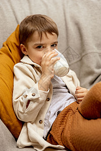 可爱的小男孩坐在家里的沙发上喝牛奶 玻璃杯中的新鲜牛奶 乳制品健康饮料 医疗保健 钙源 乳糖 穿着休闲服的学龄前儿童生态饮食食物图片