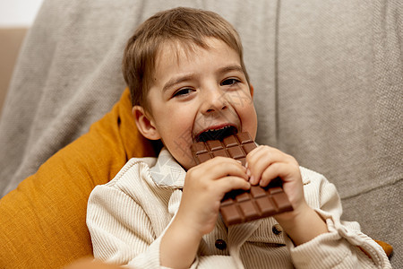 可爱的小男孩坐在家里的沙发上吃着巧克力 儿童和糖果 糖果 孩子们享用美味的甜点 穿着休闲服的学龄前儿童 积极的情绪孩子幼儿园酒吧图片