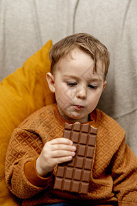 可爱的小男孩坐在家里的沙发上吃着巧克力 儿童和糖果 糖果 孩子们享用美味的甜点 穿着休闲服的学龄前儿童酒吧幼儿园饮食可可孩子产品图片