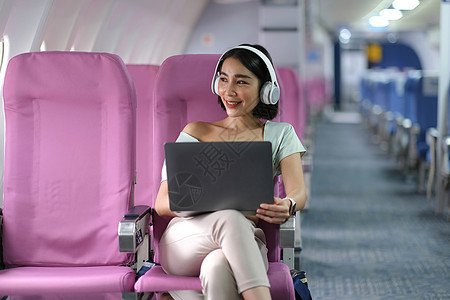 在飞行 旅行和商务概念期间 亚洲青年女子在飞机头等舱靠近窗户窗口的飞机上使用笔记本电脑戴耳机女孩男性成人工作技术女性乘客男人喷射图片