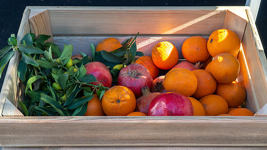 太阳光下的木箱中的橙子和石榴土图片