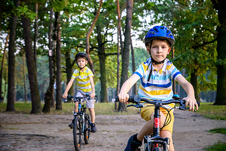 两个穿着五颜六色休闲服的小男孩在夏季森林公园骑自行车 活跃的孩子们在阳光明媚的秋日在大自然中骑自行车 安全 运动 休闲与儿童概念图片
