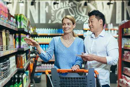 一对年轻的国际夫妇 一对女人和一个亚裔男子在超市用购物车走路图片