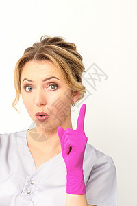 年轻的白人女医生戴着粉色手套 食指朝上 用食指做手势 我有个主意解决方案女性手臂美容师手指工作室冒充工作服女孩成人图片