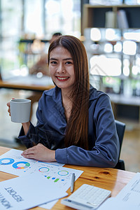 一个快乐的亚洲女人的肖像 白天咖啡休息时在她桌上微笑活动互联网幸福办公室中年人倾斜手机技术金发商务图片