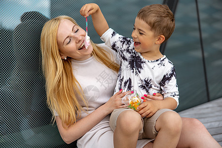快乐的金发女人和小男孩坐在露台上吃糖果 母亲和儿子一起享受时光 积极的年轻妈妈在玩耍 与她可爱的孩子共度时光 大笑 玩得开心 家图片