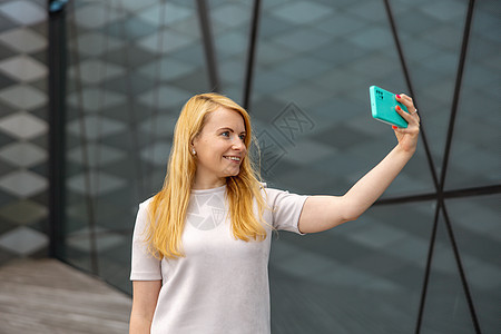 年轻的金发女人在智能手机上为她的追随者自拍 年轻有影响力的女孩 人气在网上 朋友在网上 美丽的女孩为她的社交媒体帐户制作内容拍摄图片