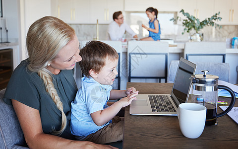 母亲 孩子和笔记本电脑坐在客厅的桌子旁 背景是父亲和女孩 在家工作的妈妈和儿子一起喝咖啡休息 儿童发展 家庭时间和放松 母亲对孩图片