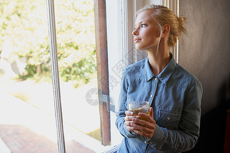 在家里放松了一天 一个年轻女人站在窗边泡茶时还冲着茶窗户成人女士咖啡杯子房子思维裁剪微笑金发女郎图片