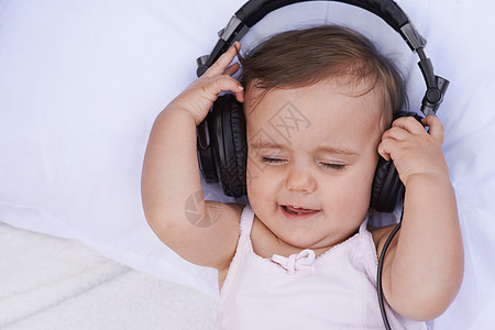 听摇篮曲 一个可爱的年轻女婴 在耳机上听音乐图片
