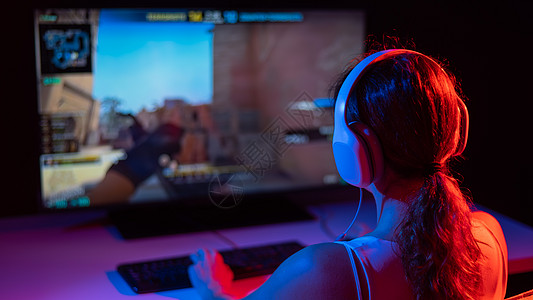 一名白人女性在黑暗中在霓虹灯下玩电脑游戏的后视图比赛竞赛视频电脑玩家游戏桌子享受键盘娱乐图片
