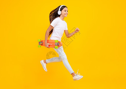 快乐的少年肖像 跳和跑 时尚少女的生活方式 漂亮的少女与滑板和耳机隔离在工作室背景 微笑着的女孩图片