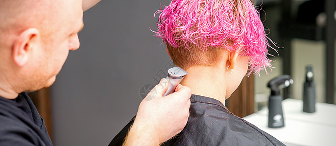男理发师在一家理发店用电动剃须机剪短的粉红色发型 为一位年轻的天主教女郎刮颈部女士店铺造型沙龙梳子脖子胡子剃刀剃须刀工人图片
