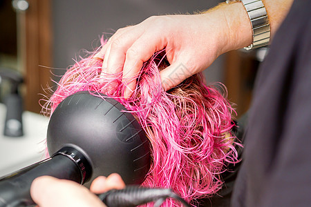 在美发沙龙 一位年轻的白人女性用黑色吹风机用刷子吹干粉红色的短鲍勃发型 特写护理烘干发刷理发师理发爆头治疗烘干机职业梳子图片