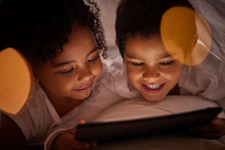 孩子们在晚上躺在床上时在数字平板电脑上学习 一起流媒体时快乐和放松 快乐的女孩和男孩醒得很晚 在室内休息时享受网络游戏和电影图片