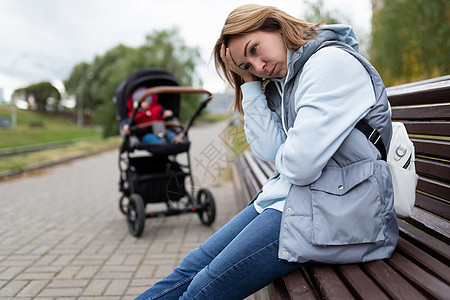 患有产后抑郁症的年轻女性母亲在公园里坐在婴儿车旁边的长椅上 内心充满了内在的感觉图片