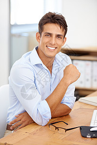一位英俊的年轻商务人士坐在他办公桌前的肖像 他很有自信图片