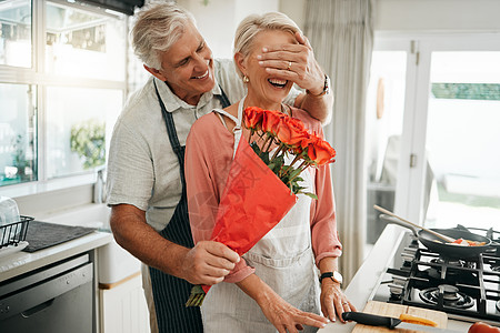 玫瑰花送给谁当男人在周年纪念日 生日或情人节那天在厨房里送给妻子一束玫瑰花时 年长夫妇会遮住眼睛和鲜花 快乐的老人和女人在澳大利亚的房子里浪背景