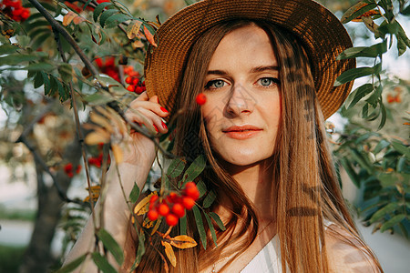 一个戴着帽子的漂亮金发女孩 留着长发 在秋季散步 一个女人在罗文树上的画像浆果季节金发女郎美甲白色草帽女士礼服头发植被图片