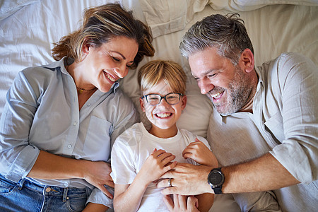 家人 挠痒痒的孩子躺在床上 他快乐的妈妈和爸爸在家里的卧室里笑着玩 男孩和一对男女父母在他们澳大利亚的房子里放松的肖像图片