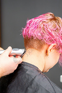 男理发师在一家理发店用电动剃须机剪短的粉红色发型 为一位年轻的天主教女郎刮颈部职业店铺梳妆台精灵沙龙男性理发女孩胡子女士图片